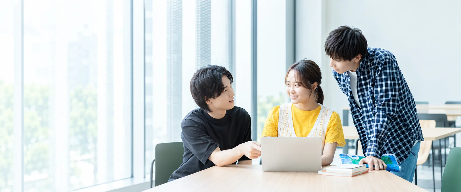 キャンパスでパソコンを囲んで話す大学生